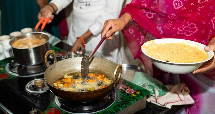 Close-up of an Indian home cook frying vegetable fritters in a brass wok on a stovetop.