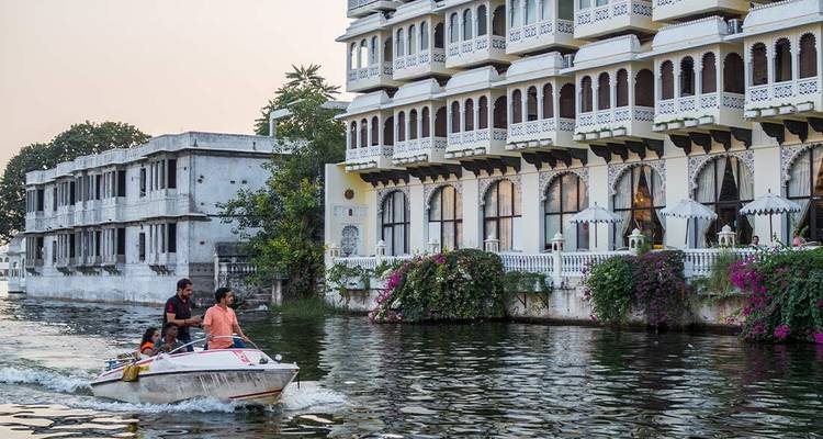 Speedboat with tourists passes a lakeside palace hotel adorned with bougainvillea in Udaipur.