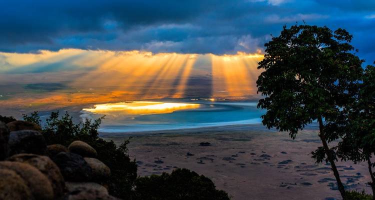 Los rayos de sol dramáticos que se abren paso entre las nubes iluminan el piso del Cráter de Ngorongoro desde un punto de vista elevado.