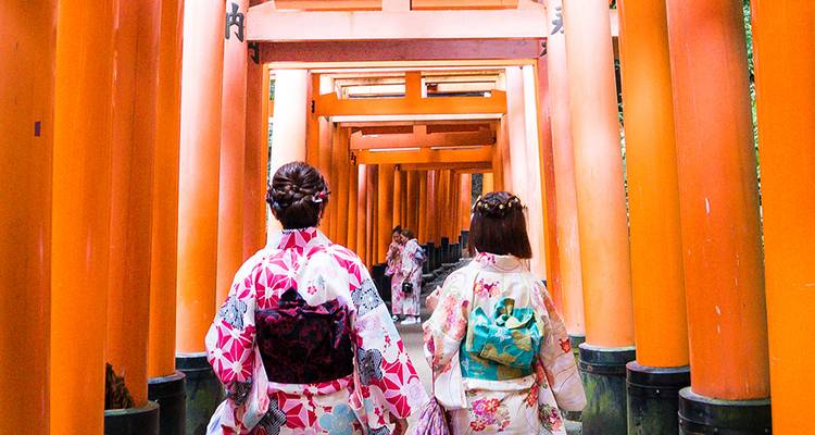 Vrouwen in kleurrijke kimono's lopen door een tunnel van levendige oranje torii poorten bij een beroemde tempel.