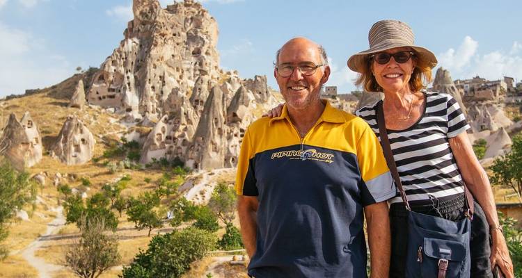 Couple souriants posant devant les cheminées rocheuses uniques de la Cappadoce sous un ciel lumineux.