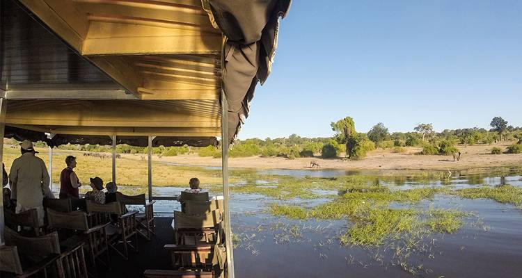 Les passagers d'une croisière fluviale en safari scrutent la plaine inondable lointaine à la recherche de la faune sous un ciel dégagé.
