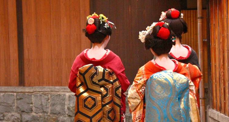 Vue arrière de trois maiko vêtues de kimonos marchant dans une ruelle traditionnelle à Kyoto.