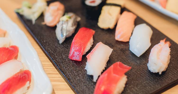 Assortiment van kleurige nigiri sushi stukjes netjes gerangschikt op een zwart serveerbord.
