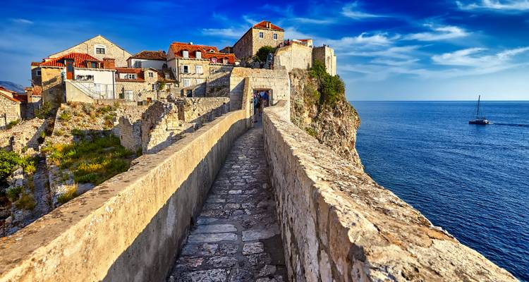 Allée pavée en pierre au sommet des anciens remparts de Dubrovnik dominant la mer Adriatique sous un ciel bleu éclatant.