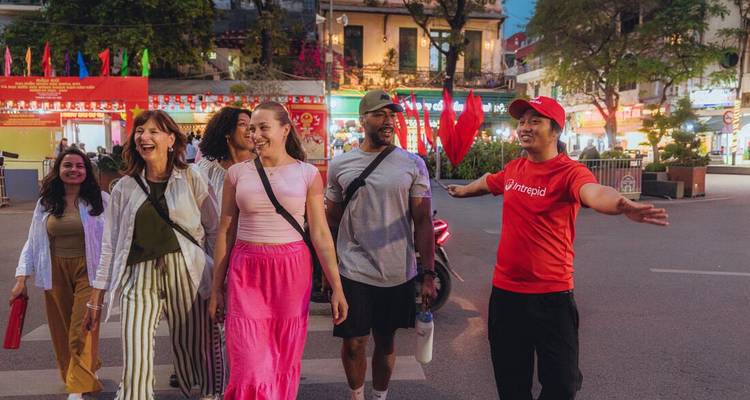 Group walks through a lively city street led by a guide holding a red flag.