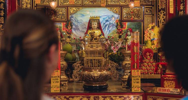 Blurred travellers observe an ornate shrine filled with gold and red decorations.