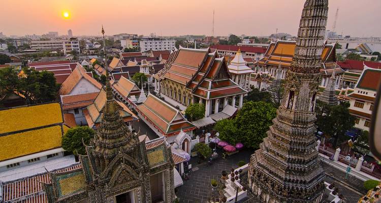Gouden zonsondergang over Bangkok met sierlijke tempelspitsen en kleurrijke daken gezien van bovenaf.