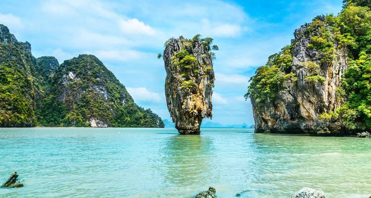 Dramatische kalkstenen karstformaties die verticaal uit smaragdgroen zeewater omhoog rijzen, omgeven door jungle-bedekte rotsen in een zonnige baai