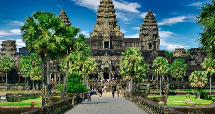 Frontale benadering van Angkor Wat met een met palmen omzoomde doorgang en majestueuze stenen torens onder een diepblauwe hemel.