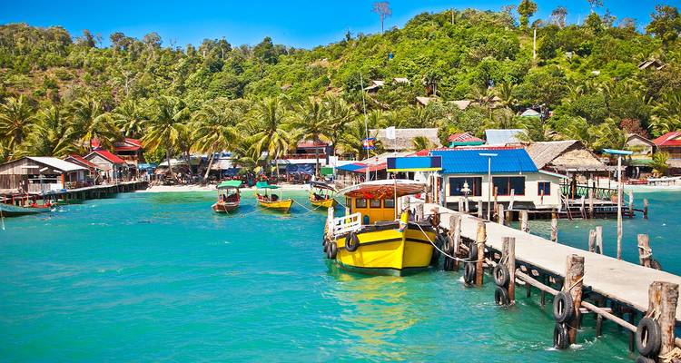Kleurrijk vissersdorpje en boten aangemeerd in een levendige turquoise tropische baai met weelderig oerwoud op de achtergrond.