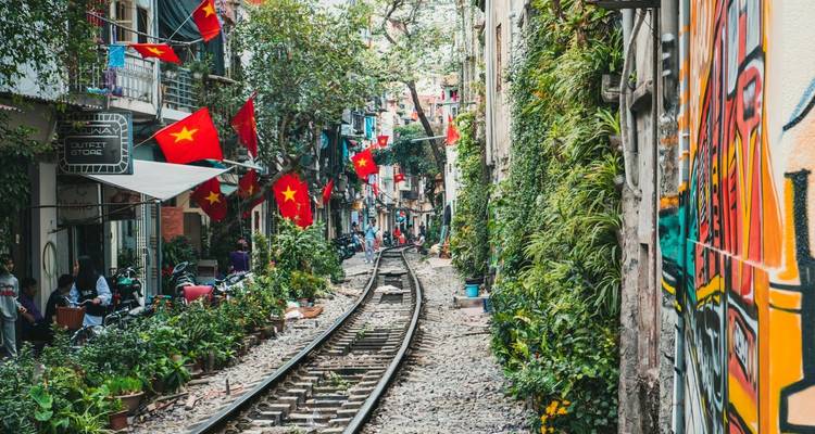 Voie ferrée traversant une étroite rue résidentielle bordée de drapeaux vietnamiens et de balcons verdoyants