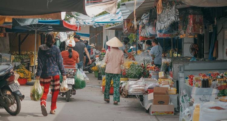 Callejón del mercado local al aire libre con vendedores, compradores y puestos llenos de productos y artículos