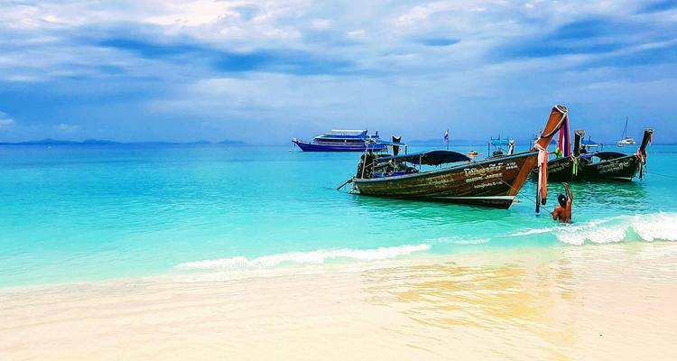 Los tradicionales barcos de cola larga flotan en un mar turquesa cristalino bajo cielos azules dramáticos