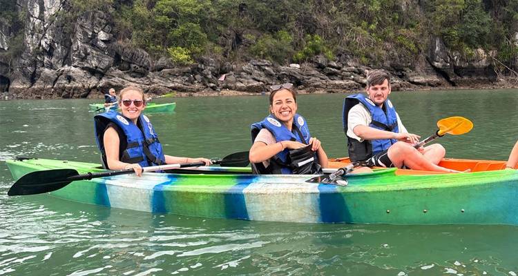 Tres viajeros en kayaks sonríen mientras reman en aguas verdes enmarcadas por acantilados de piedra caliza