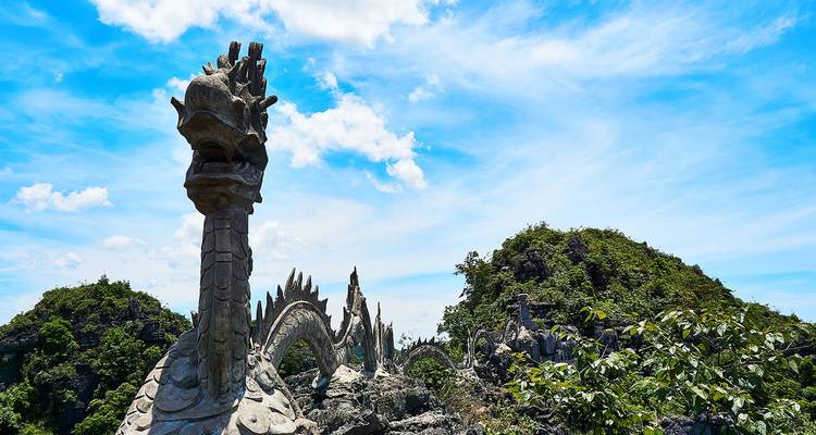 La escultura de dragón de piedra se serpentea a lo largo de una cresta de montaña rocosa bajo un cielo azul brillante