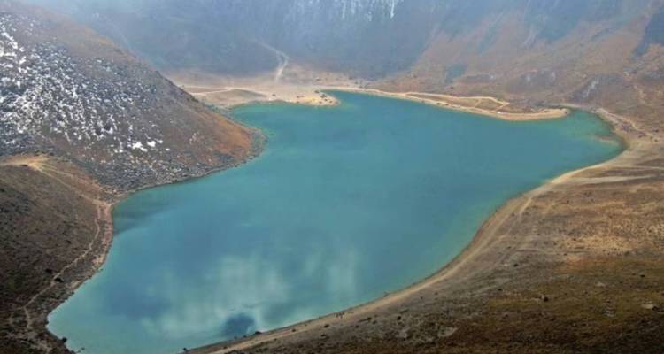 High vantage view of a turquoise crater lake surrounded by barren volcanic slopes and patches of snow.