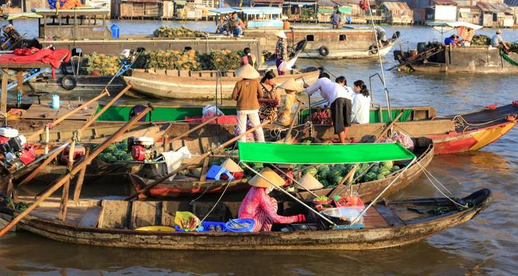 Colorful wooden boats crowded with vendors trading goods at a lively floating market on a muddy river.