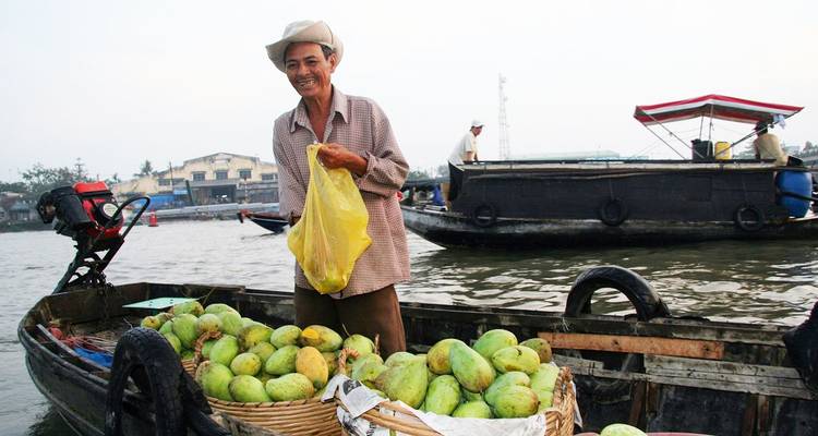 Lächelnder Verkäufer auf einem Holzboot, der Körbe mit grünen Mangos auf einem Schwimmmarkt verkauft