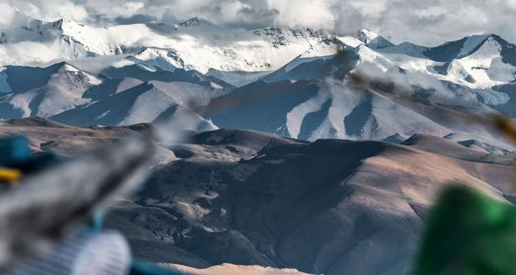 Layered view of jagged snow-peaked mountains and barren ridges under swirling clouds.