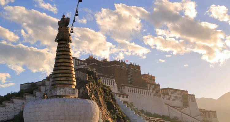Potala Palace rises on a hill beside a golden chorten, lit by warm evening light and a cloudy sky.