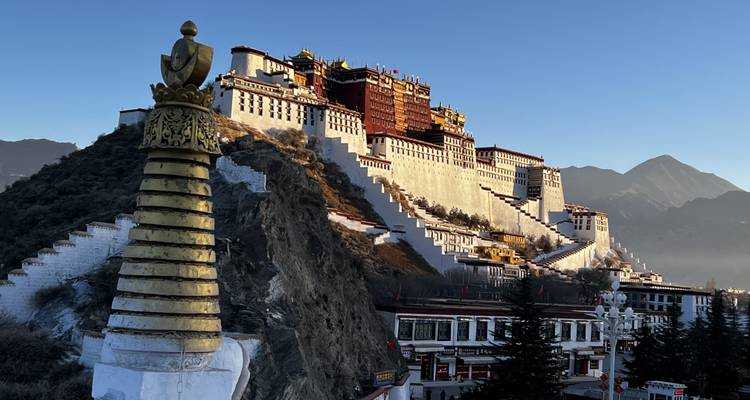 Clear sunrise view of Potala Palace and golden stupa against a deep blue sky and distant mountains.