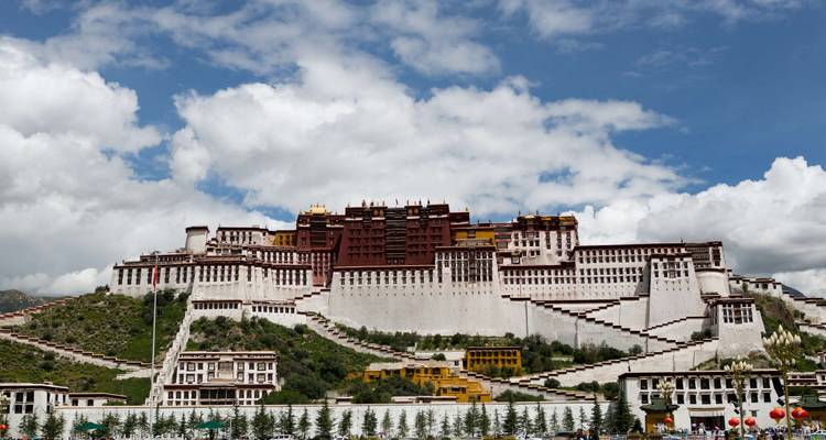 Potala Palace stands majestically under a bright blue sky dotted with white clouds.