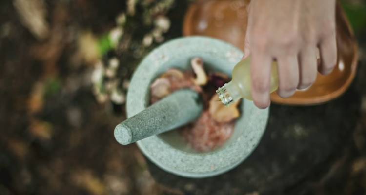 Close-up of hand pouring essential oil into a stone mortar with natural spa ingredients.