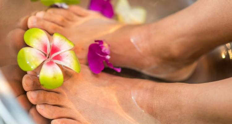 Feet soaking in a floral foot bath with floating orchids and green apple blossom at a spa.