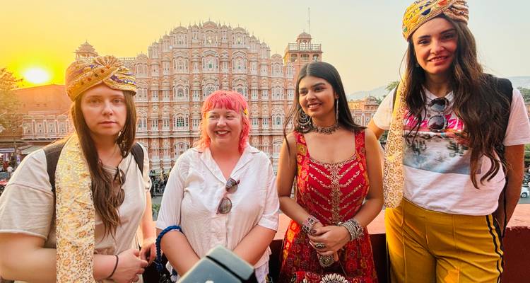 Group of women in traditional headwear standing on a terrace with Hawa Mahal at sunset