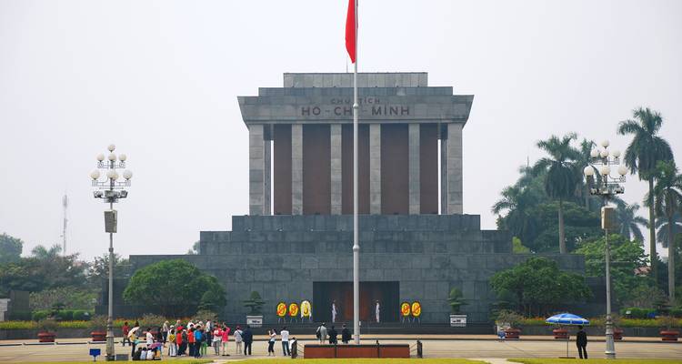 Frontansicht des strengen Granitgrabes von Ho Chi Minh mit einer vietnamesischen Flagge und einer Reisegruppe, die sich auf dem Platz versammelt hat.