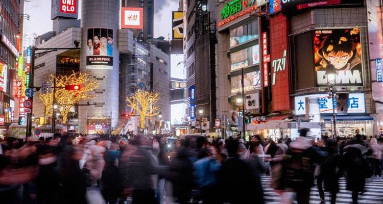 Bustling neon Shibuya crossing packed with blurred crowds and towering LED billboards at night.