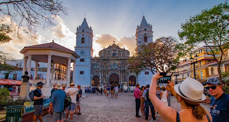 Vibrant street scene in Panama City's historic quarter with a baroque cathedral at sunset and tourists milling about.