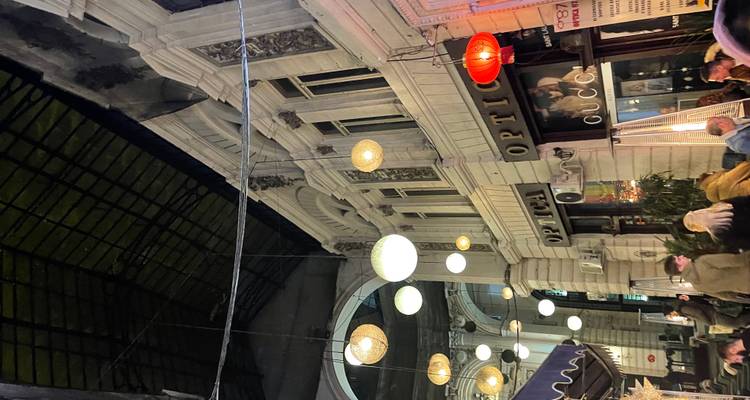 Overdekte arcade met hangende lantaarns en kleine cafés, gasten zittend buiten in de avond