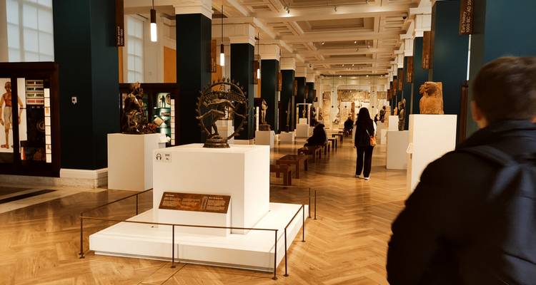 Interior gallery of the British Museum with sculptures and visitors along polished floor.