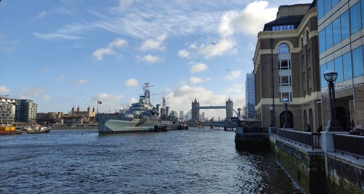 River Thames vista featuring HMS Belfast and Tower Bridge in the distance under blue sky.