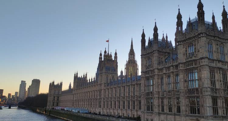 Evening light on the Houses of Parliament stretching along the riverbank with city skyline beyond.