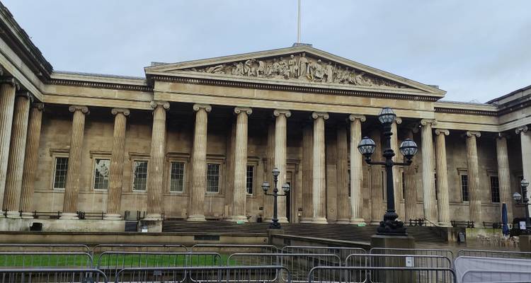 Classical façade of the British Museum with tall columns and barriers in front.