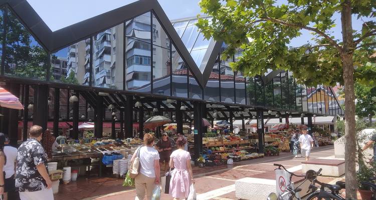 Zonnige dag op de verse markt van Tirana met een modern reflecterend dak en winkelende mensen