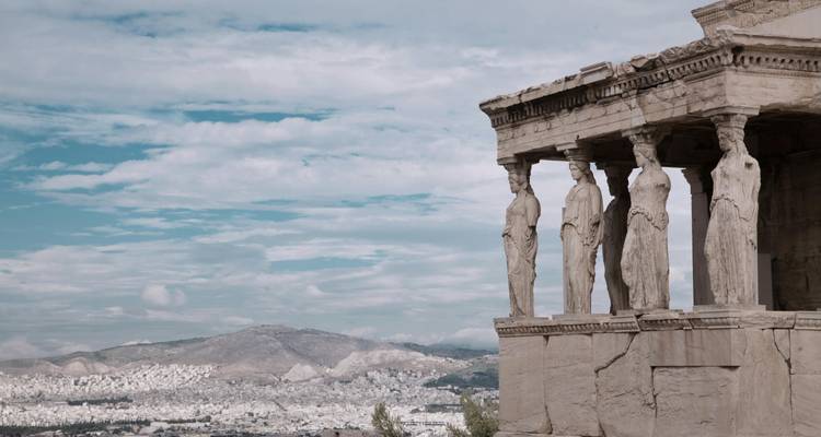 Caryatid figures of the Erechtheion with a panoramic backdrop of Athens and distant mountains.