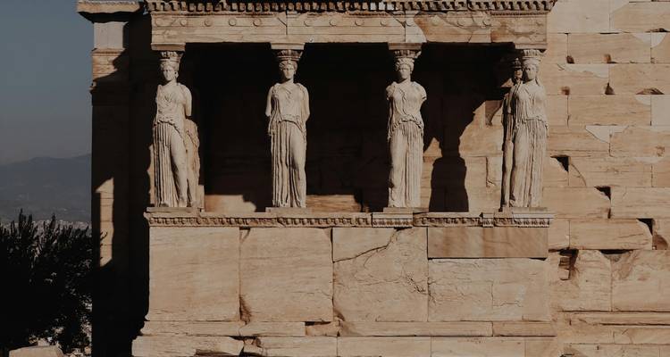 Side-lit Caryatids on the Erechtheion porch casting strong shadows on the ancient stone.