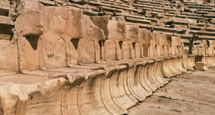 Close-up of weathered marble seats in an ancient Greek theatre showing inscriptions and texture.