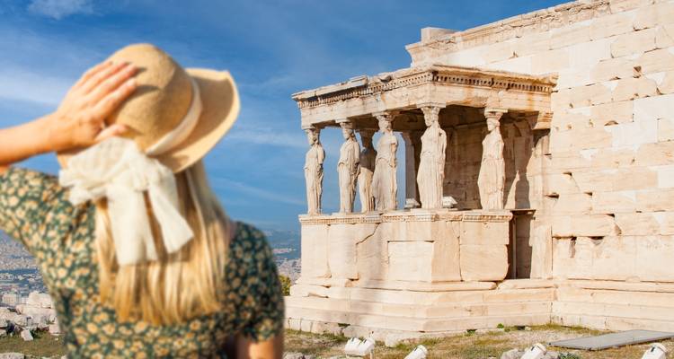 Female traveller in sunhat admiring the Caryatids of the Erechtheion under a blue sky.