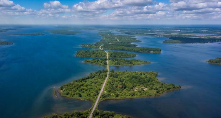 Vue aérienne d'une succession d'îles verdoyantes et d'une route-chaussée entourées par les eaux bleues de la région des Mille-Îles.