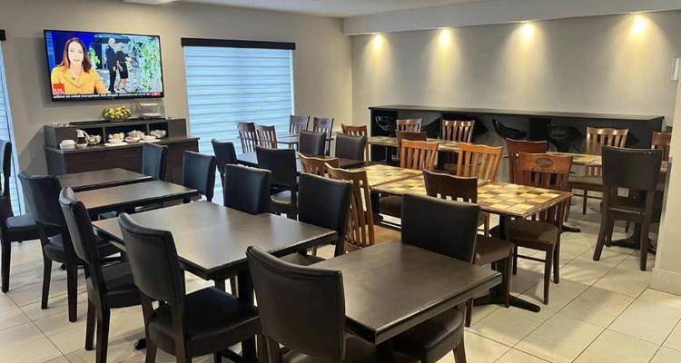 Simple hotel breakfast area with dark wooden tables, chairs, and a TV on one wall.
