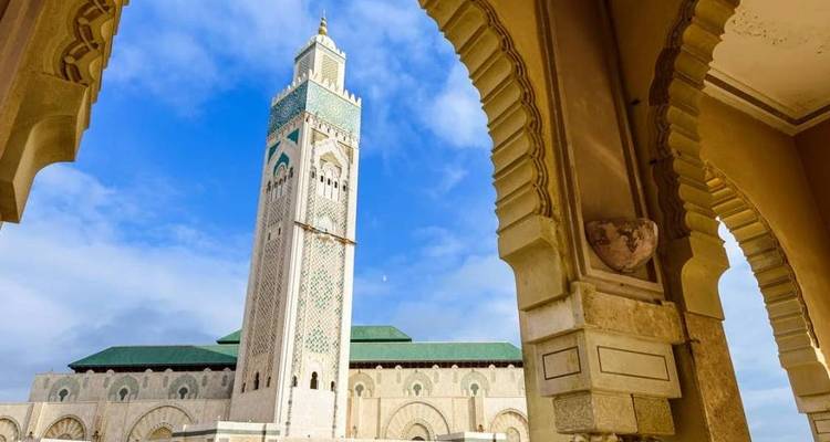The Hassan II Mosque minaret soars into a vivid blue sky, perfectly framed by ornate arches.