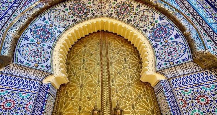 An ornate golden door framed by intricate zellige tile work and arches showcases Moroccan craftsmanship.