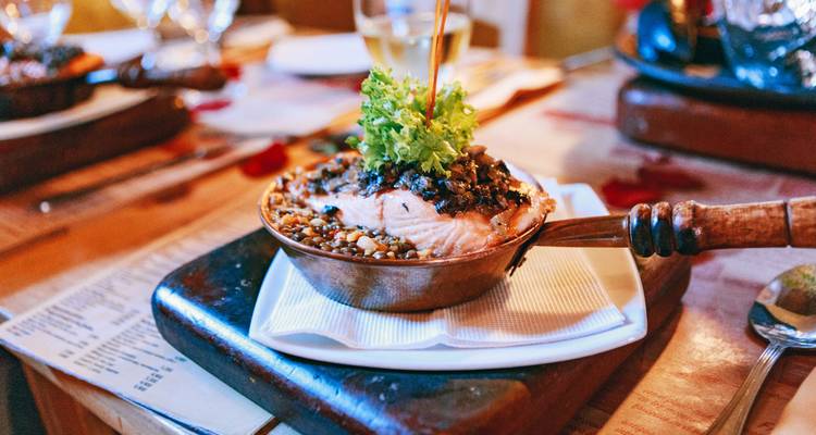 Close-up of an appetising salmon dish garnished with greens and served in a small copper pan.