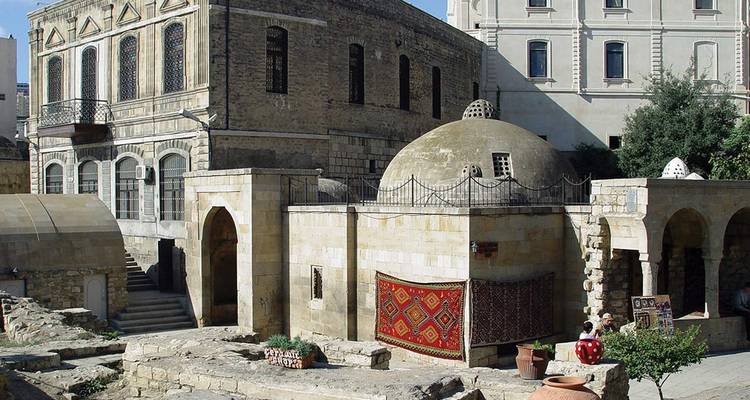 Historic stone bathhouse and surrounding architecture with colourful carpet hung on a wall.