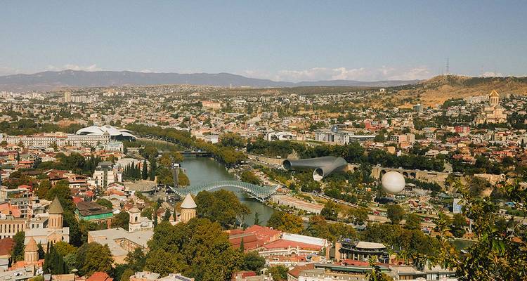 Panoramic cityscape of Tbilisi featuring the curving Peace Bridge and the Mtkvari River.